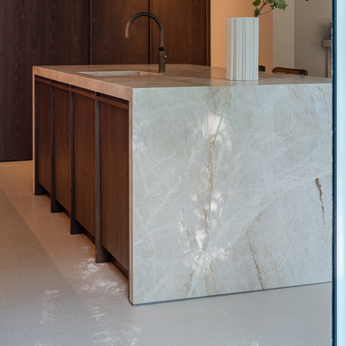 Keuken met Zilva Barosso gietvloer en luxe marmeren kookeiland. Zilva Barosso gietvloer met marmerkorrels in keuken met marmeren kookeiland en houten elementen.