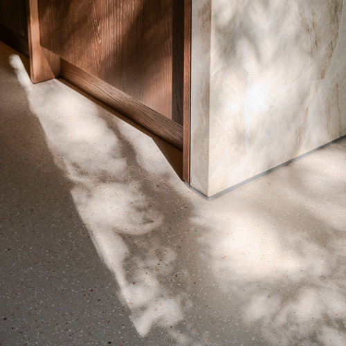 Natuurlijke lichtinval op Zilva Barosso gietvloer met marmerkorrels in keuken. Natuurlijke schaduw op de Zilva Barosso gietvloer met marmerkorrels naast een marmeren keukenblok.